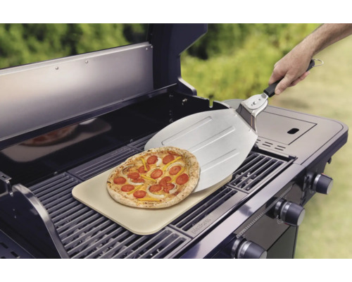 Pizza på en pizzasten på en grill med en pizzaspade