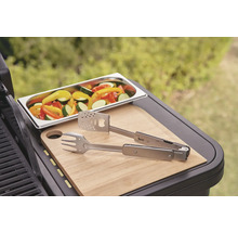Grönsaker i en skål, grilltång och skärbräda på en grill