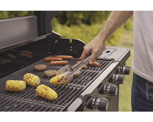 Grill med grillade produkter som majskolvar, korvar och hamburgare, en person använder en grilltång.