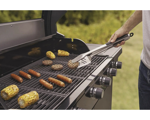 Grill med grillade korvar, hamburgare och majskolvar, som hanteras med grillverktyg