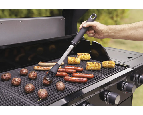 Grillscen med grillborste, korvar, majskolvar och köttbullar på en gasolgrill.