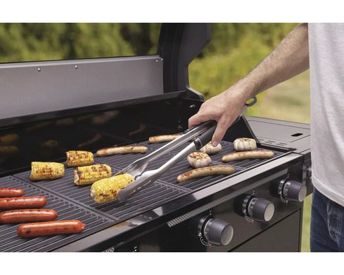 Grill med majskolvar, korv och vitlök på gallret och en person med grilltång.