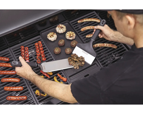 Man grillar korv, grönsaker och vitlök på en grill med grillspatlar.