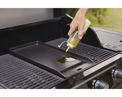 En person häller olja på en grillplatta på en gasolgrill.
