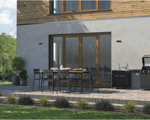 Terrass med matbord, stolar, diskho och grill framför ett hus.