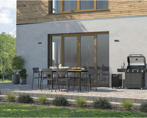 Uteplats med gasolgrill, trädgårdsbord och stolar framför ett hus