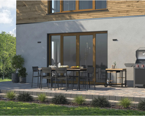 Uteplats med matbord, stolar, grill och grillvagn framför ett hus