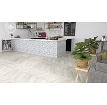 Interiörbild av ett kafé med trägolv i fiskbensmönster, en bänk med mönstrade plattor och krukväxter