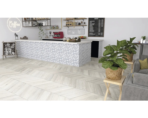 Interiörbild av ett kafé med trägolv i fiskbensmönster, en bänk med mönstrade plattor och krukväxter