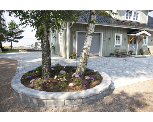 Uppfart med gatsten, omgiven av en mur och planterad med blommor