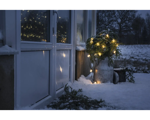 Vinterscen utomhus med upplysta granar framför en ytterdörr i snön