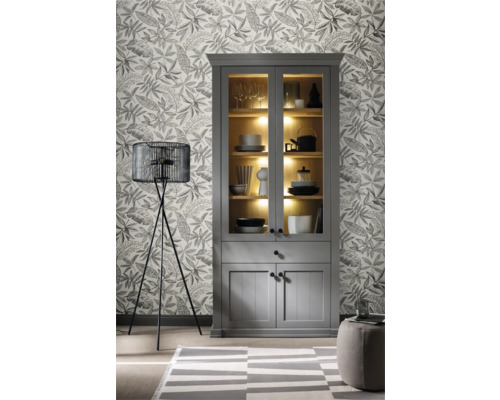 Vardagsrum med grått vitrinskåp, golvlampa och mönstrad tapet.