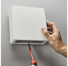 Installation av en vit vägglampa med en skruvmejsel