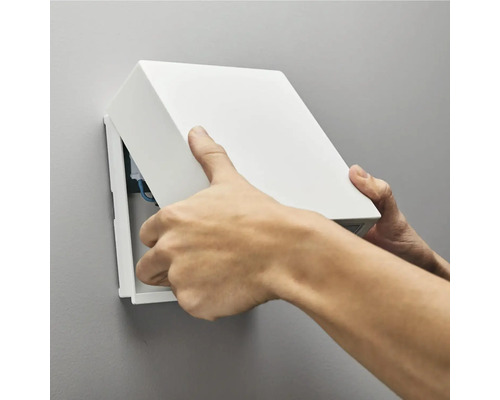 En man öppnar en kopplingsdosa på en vägg.