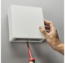 Montering av en vit vägglampa med en skruvmejsel.