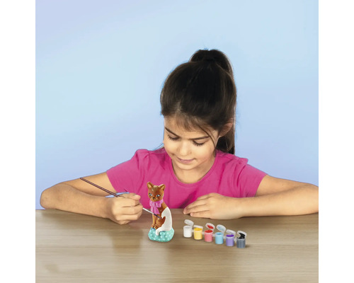 Flicka målar en kattstaty med penslar och färger.
