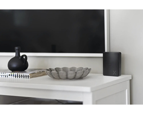 Dekorativa föremål och elektronisk apparat på en vit skänk framför en TV.