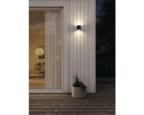 Exteriör av ett hus med en modern vägglampa som lyser upp en terrass