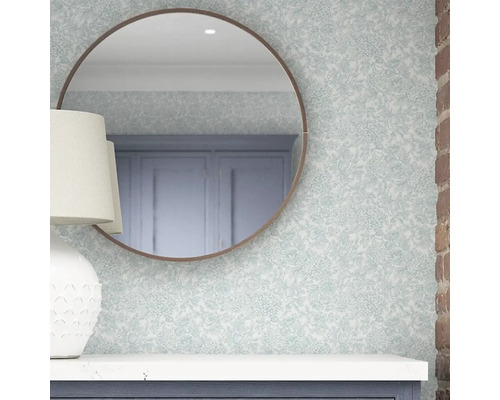Rund spegel hänger på en vägg med blommönster ovanför ett skåp.