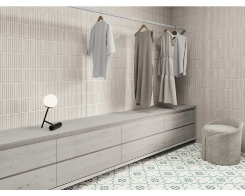 Ljust omklädningsrum med kakelvägg, byrå, pall och klädstång med kläder