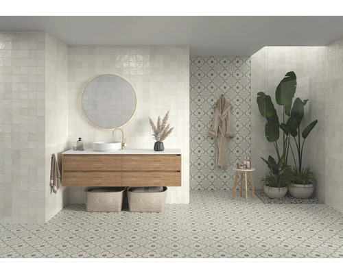 Ljust badrum med fyrkantiga väggplattor, tvättställsskåp med spegel och mönstrade golvplattor