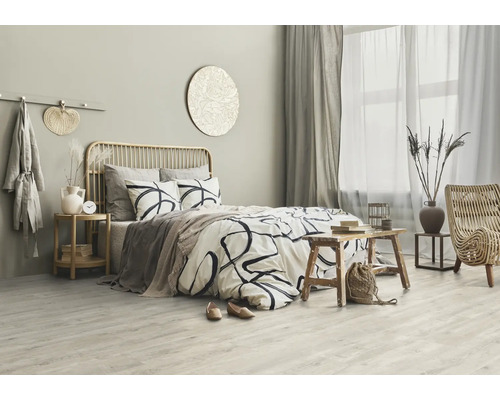 Ljust sovrum med säng, sidobord i trä och rottingfåtölj