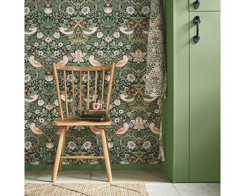 Rumsutsikt med blommönstrad tapet, trästol, bokstapel och matchande gardin.