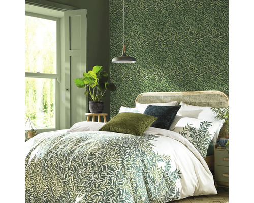 Sovrum med säng, sängbord, krukväxt och grön tapet med bladmönster.
