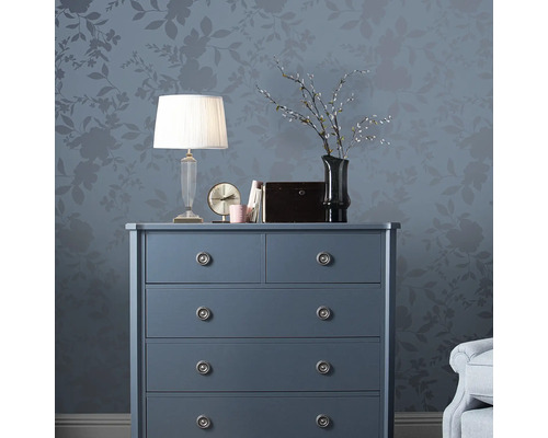 Byrå med lampa, klocka och dekoration framför en vägg med blommönster