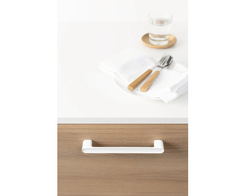 Detaljbild av ett skåp med vitt handtag, ovanför ett dukat bord med bestick och ett glas vatten