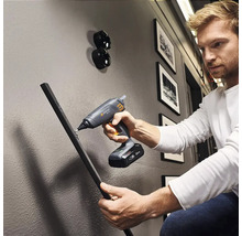 En man använder en sladdlös limpistol för att fästa ett arbetsstycke på en vägg.