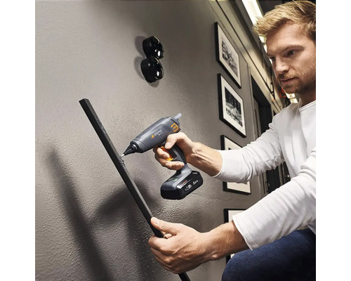 En man använder en sladdlös limpistol för att fästa ett arbetsstycke på en vägg.