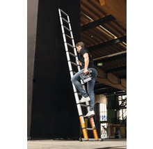 Man klättrar på en teleskopisk stege med ett elverktyg i handen.