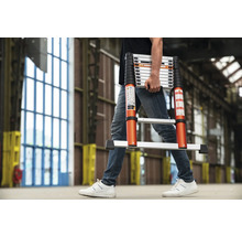 En person bär en teleskopisk stege i en interiör.