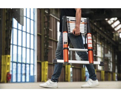 En person bär en teleskopisk stege i en interiör.