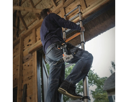 Hantverkare på en teleskopstege med en batteridriven skruvdragare i bältet på jobbet.