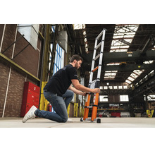 En person justerar en teleskopisk aluminiumstege i ett lager.