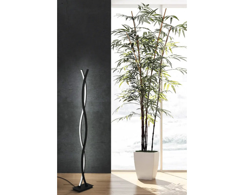 Modern golvlampa med böjd design och LED-belysning bredvid en krukväxt i ett ljust rum.