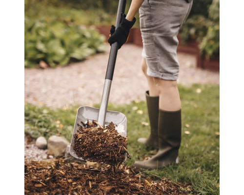 En person som skyfflar barkmull med en spade i trädgården.