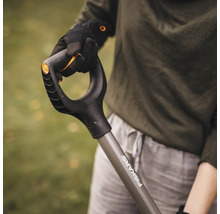 En person håller en spade av märket Fiskars.