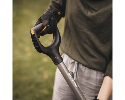 En person håller en spade av märket Fiskars.