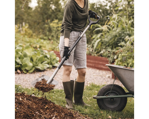Kvinna använder spade för att flytta mulch i en trädgård.