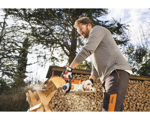 En man sågar trä med en motorsåg utomhus framför en vedförvaring.