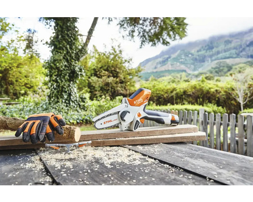 Batteridriven motorsåg med skyddshandskar på träbord i trädgården