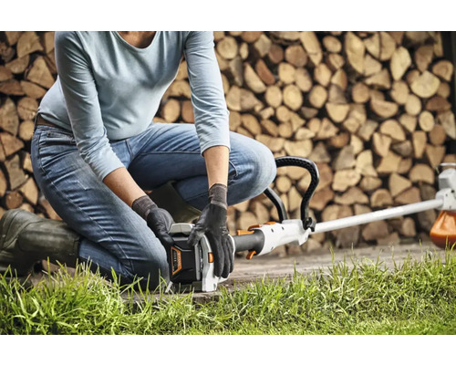 En person hukar sig ner för att använda en grästrimmer framför en stapel ved.