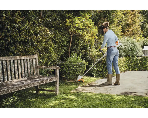 En kvinna trimmar gräs med en grästrimmer i en trädgård.