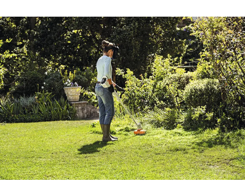Kvinna arbetar med en batteridriven grästrimmer i trädgården