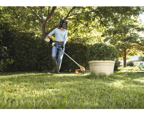 En kvinna använder en grästrimmer i trädgården.