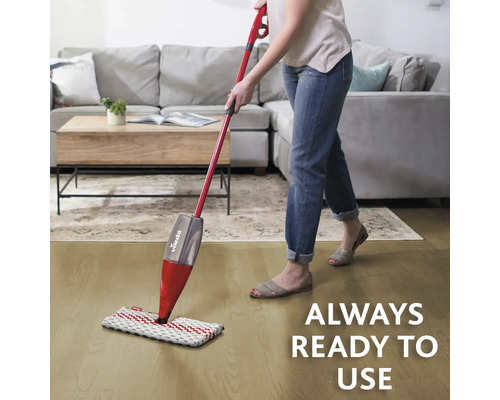 Kvinna moppar golvet med en Vileda mopp framför en soffa