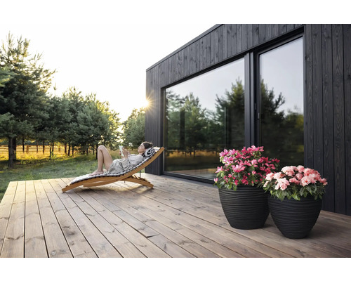 "Scen med kvinna som kopplar av på en solstol i trä på en träterrass framför ett hus med stora fönster